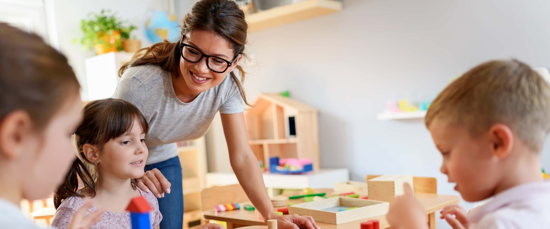 Vorschullehrerin mit Kindern, die mit bunten Holzfiguren spielen