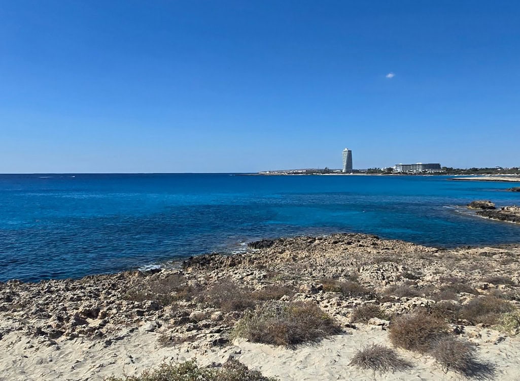 Küstenlandschaft mit klarem blauem Meer, hellem Himmel und Felsen im Vordergrund.